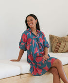 Woman wearing short loose blue dress with elbow length sleeves and large pink and red floral print.