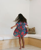 Woman wearing short loose blue dress with elbow length sleeves and large pink and red floral print.