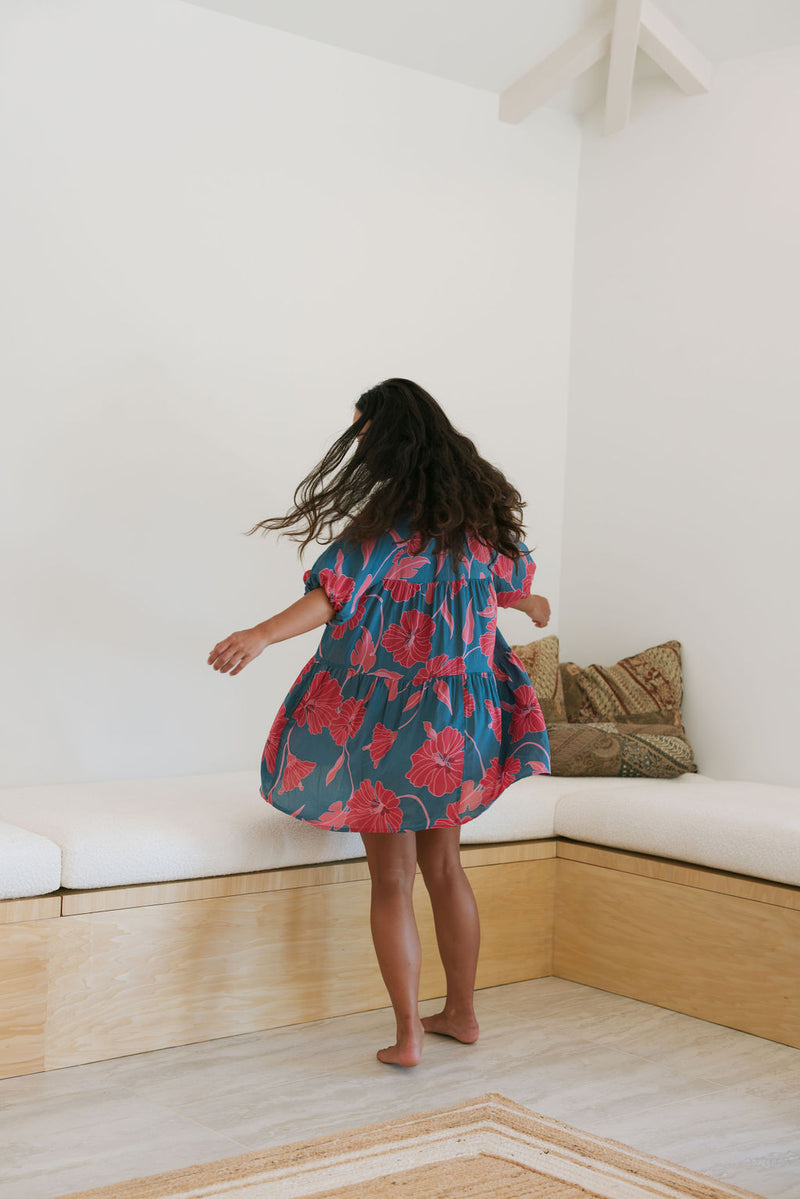 Woman wearing short loose blue dress with elbow length sleeves and large pink and red floral print.