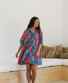 Woman wearing short loose blue dress with elbow length sleeves and large pink and red floral print.