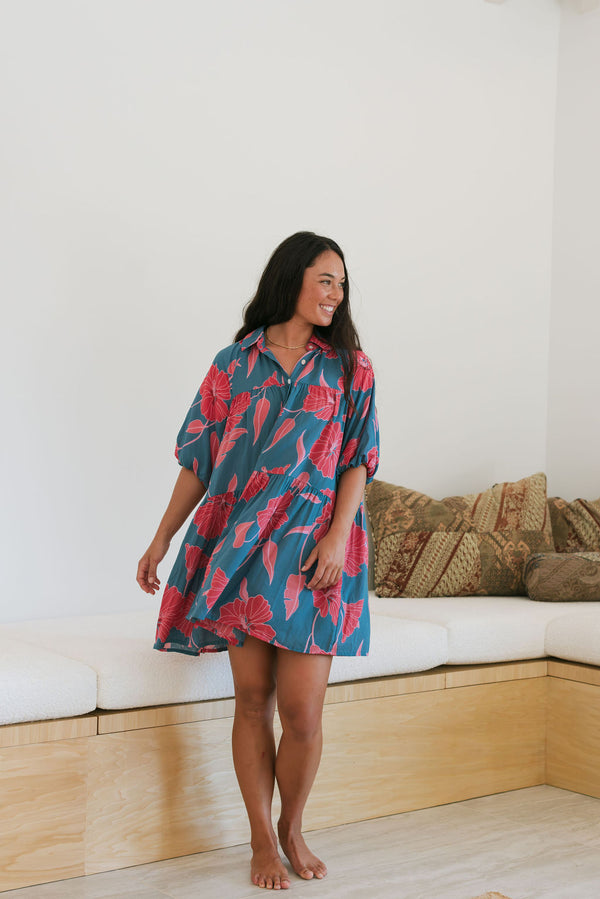 Woman wearing short loose blue dress with elbow length sleeves and large pink and red floral print.