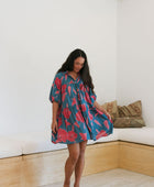 Woman wearing short loose blue dress with elbow length sleeves and large pink and red floral print.