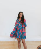 Woman wearing short loose blue dress with elbow length sleeves and large pink and red floral print.