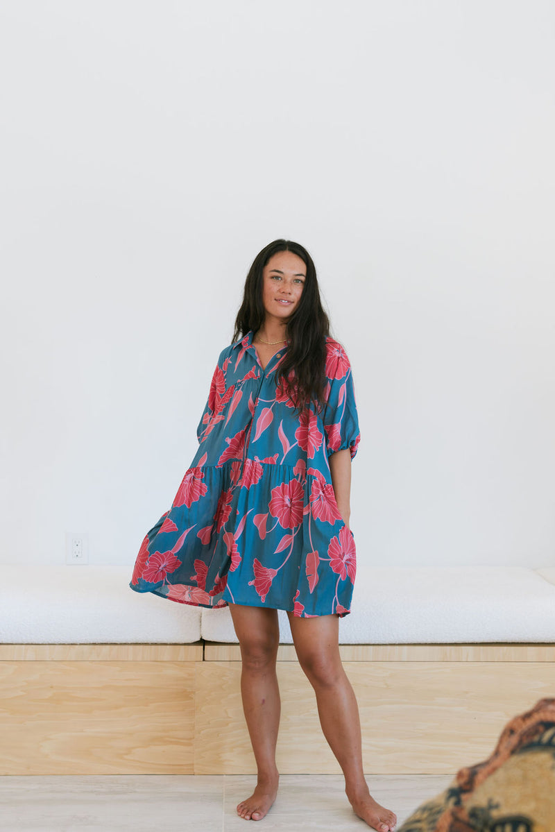 Woman wearing short loose blue dress with elbow length sleeves and large pink and red floral print.