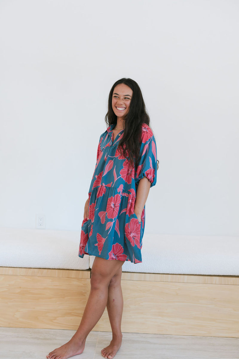 Woman wearing short loose blue dress with elbow length sleeves and large pink and red floral print.