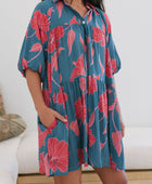 Woman wearing short loose blue dress with elbow length sleeves and large pink and red floral print.