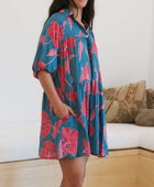 Woman wearing short loose blue dress with elbow length sleeves and large pink and red floral print.