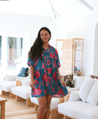 Woman wearing short loose blue dress with elbow length sleeves and large pink and red floral print.