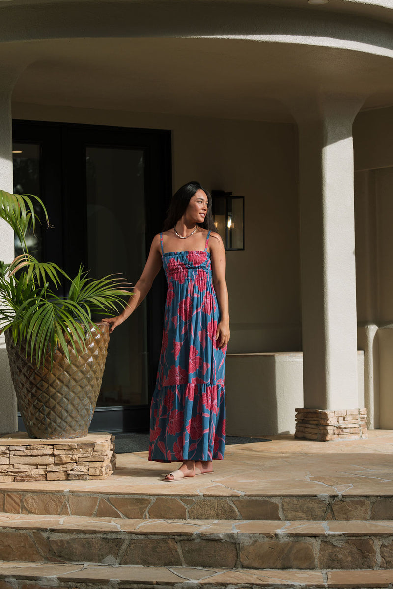 Woman wearing blue sleeveless maxi dress with large pink and red floral print.