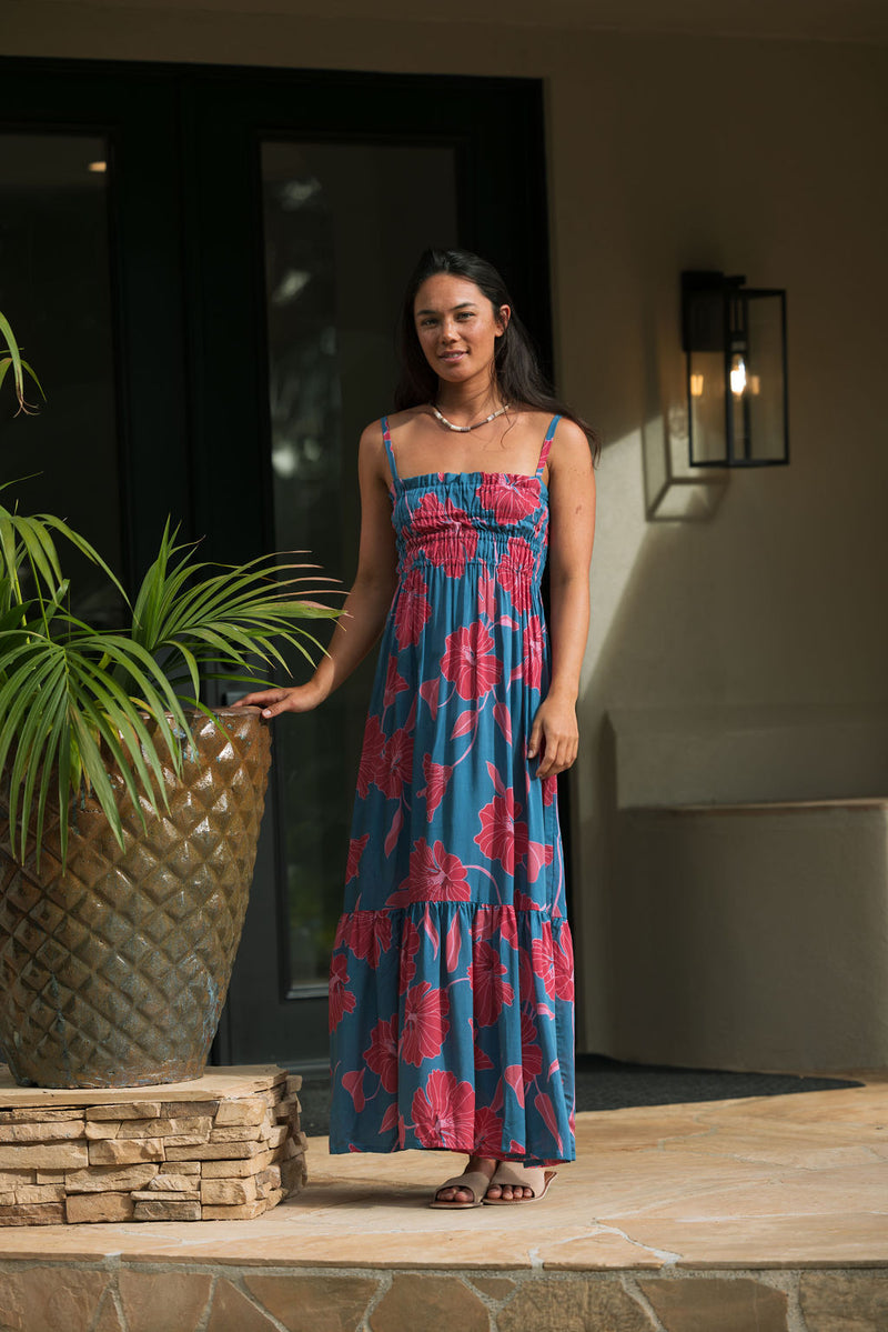 Woman wearing blue sleeveless maxi dress with large pink and red floral print.