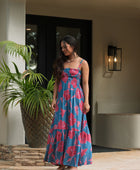 Woman wearing blue sleeveless maxi dress with large pink and red floral print.