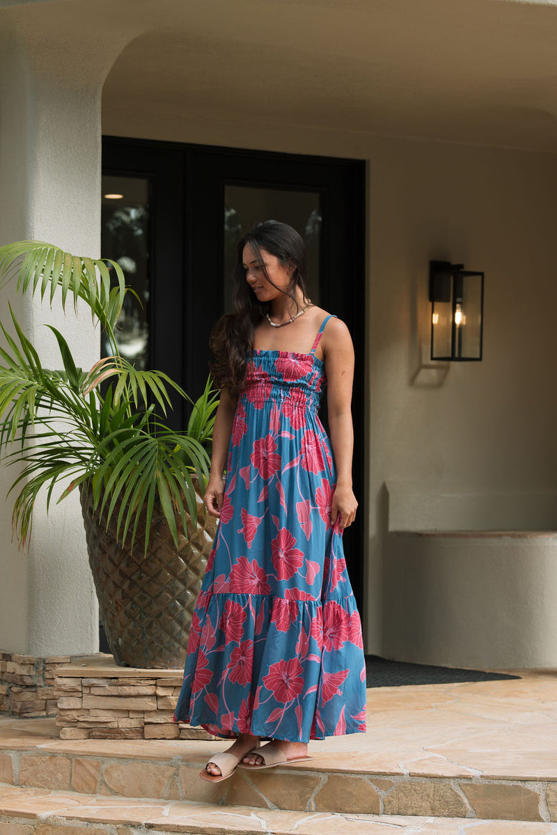 Woman wearing blue sleeveless maxi dress with large pink and red floral print.