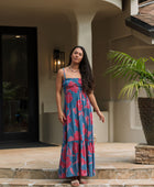 Woman wearing blue sleeveless maxi dress with large pink and red floral print.