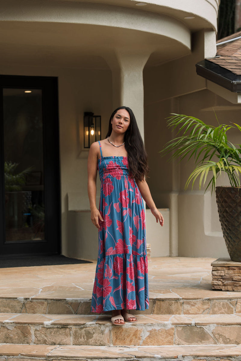 Woman wearing blue sleeveless maxi dress with large pink and red floral print.