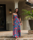 Woman wearing blue sleeveless maxi dress with large pink and red floral print.