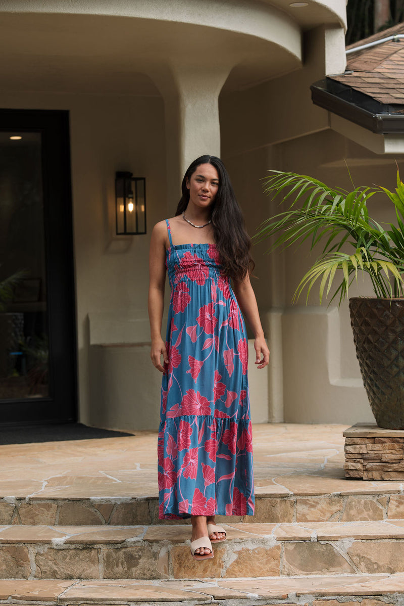 Woman wearing blue sleeveless maxi dress with large pink and red floral print.