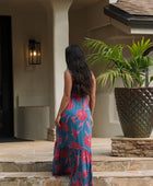 Woman wearing blue sleeveless maxi dress with large pink and red floral print.