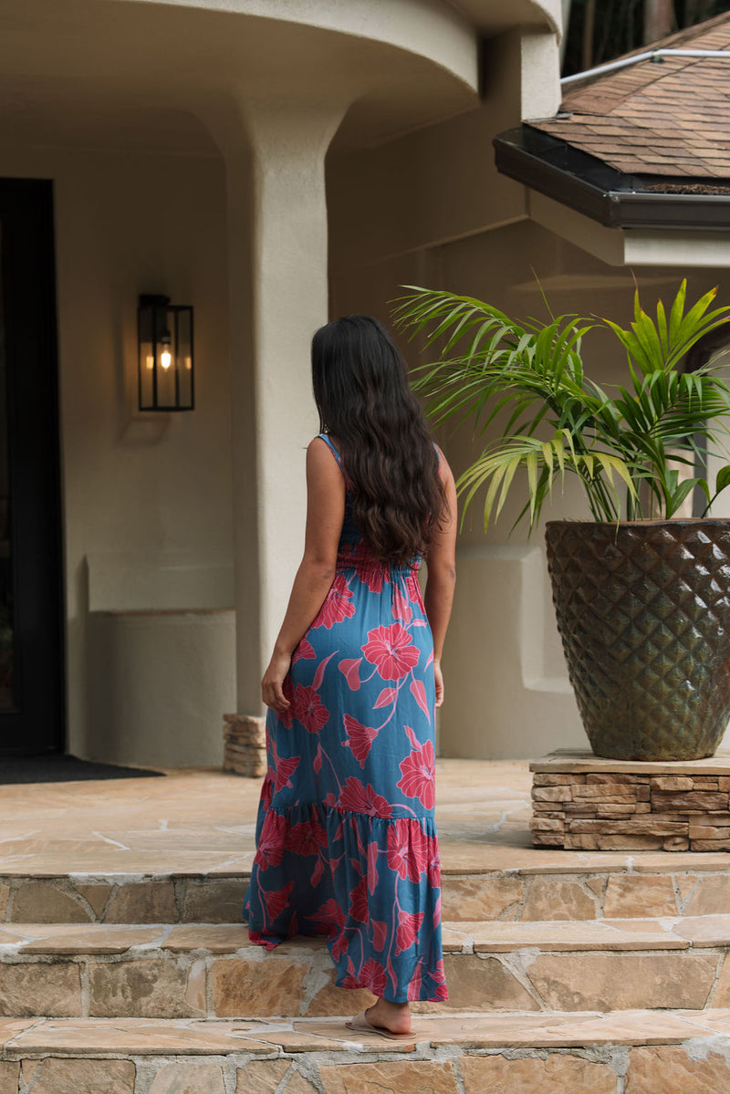 Woman wearing blue sleeveless maxi dress with large pink and red floral print.