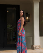 Woman wearing blue sleeveless maxi dress with large pink and red floral print.