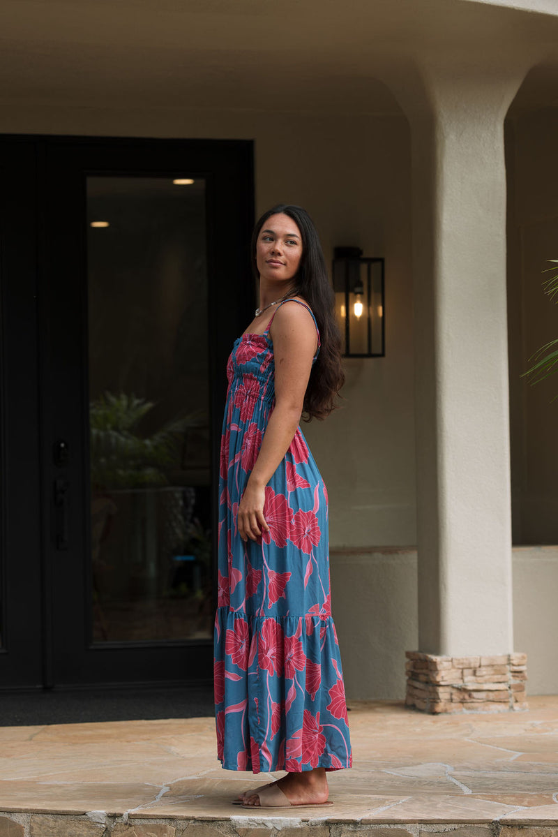 Woman wearing blue sleeveless maxi dress with large pink and red floral print.