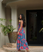 Woman wearing blue sleeveless maxi dress with large pink and red floral print.