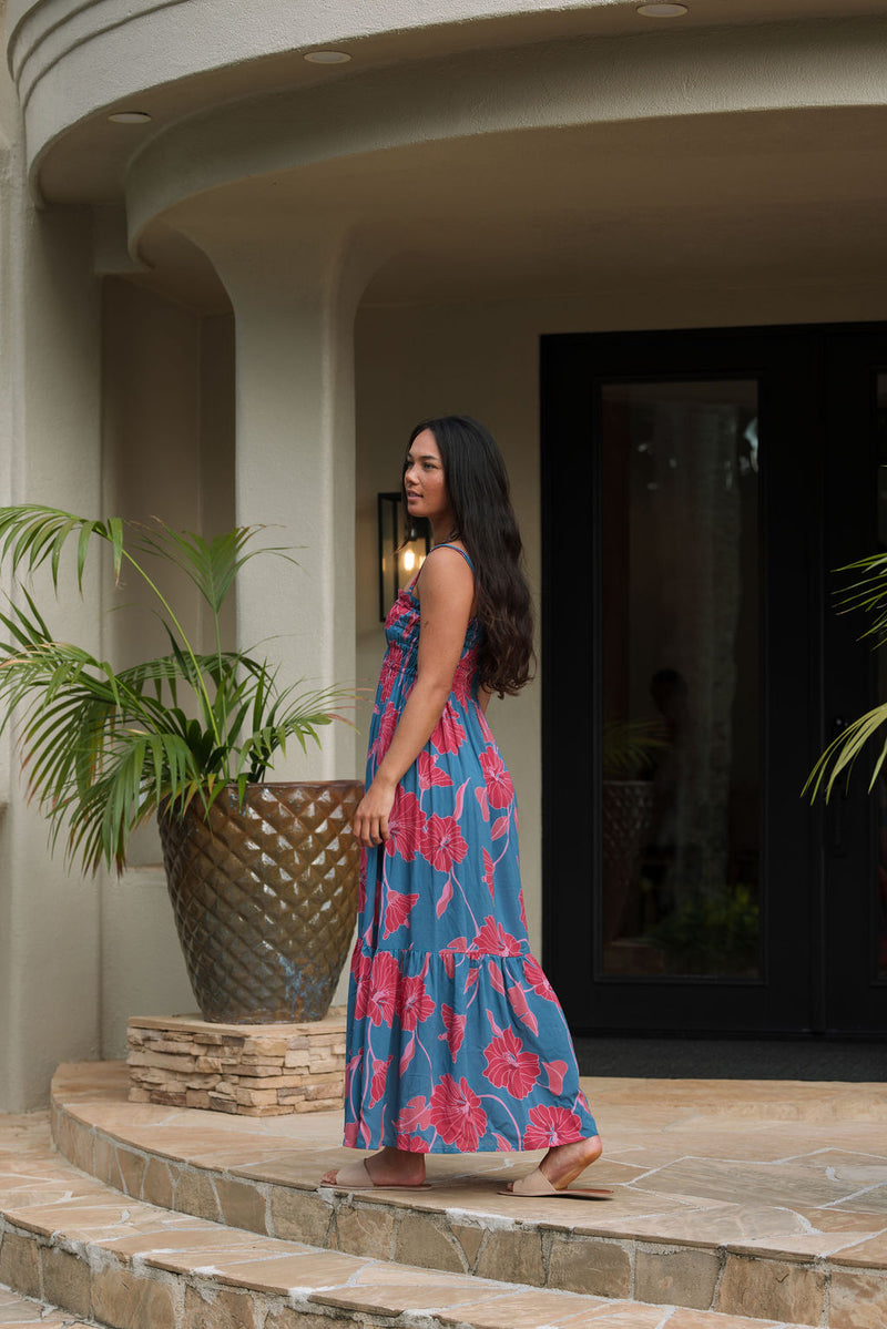 Woman wearing blue sleeveless maxi dress with large pink and red floral print.