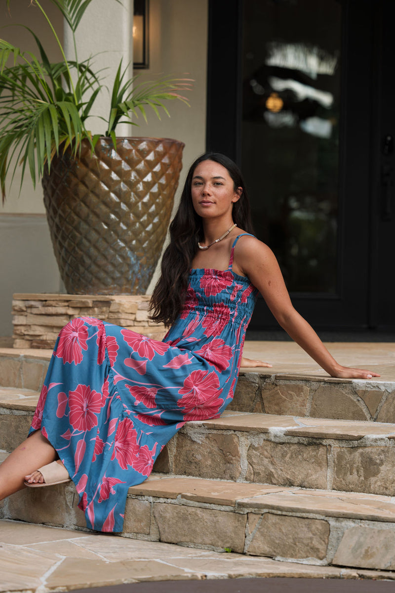 Woman wearing blue sleeveless maxi dress with large pink and red floral print.