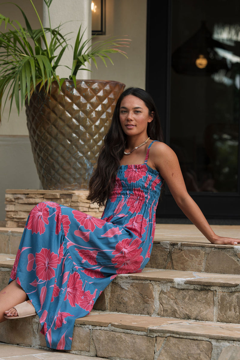 Woman wearing blue sleeveless maxi dress with large pink and red floral print.