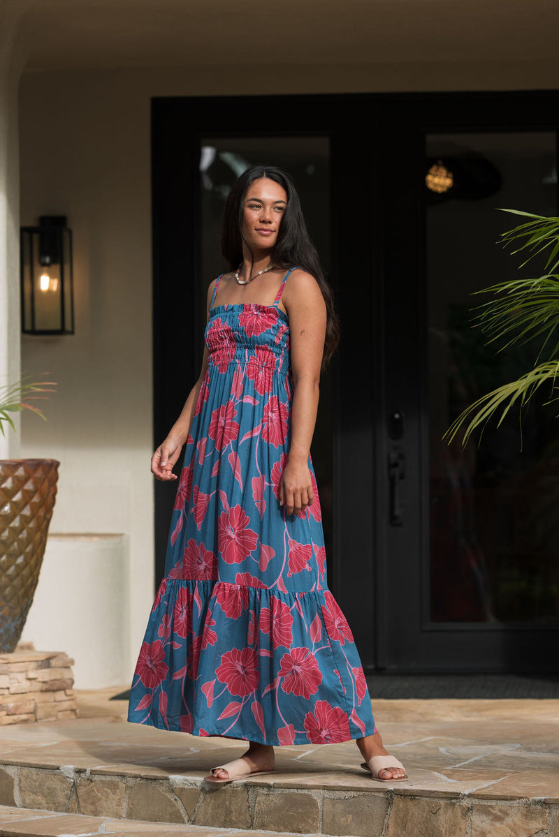 Woman wearing blue sleeveless maxi dress with large pink and red floral print.