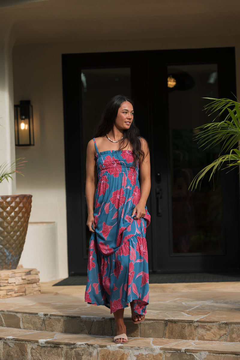 Woman wearing blue sleeveless maxi dress with large pink and red floral print.