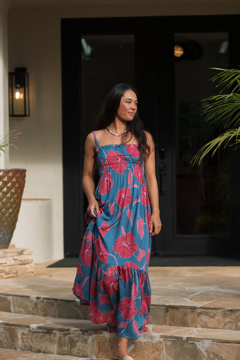 Woman wearing blue sleeveless maxi dress with large pink and red floral print.