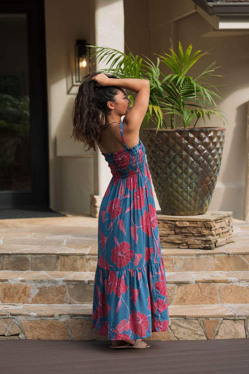 Woman wearing blue sleeveless maxi dress with large pink and red floral print.