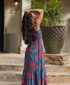 Woman wearing blue sleeveless maxi dress with large pink and red floral print.