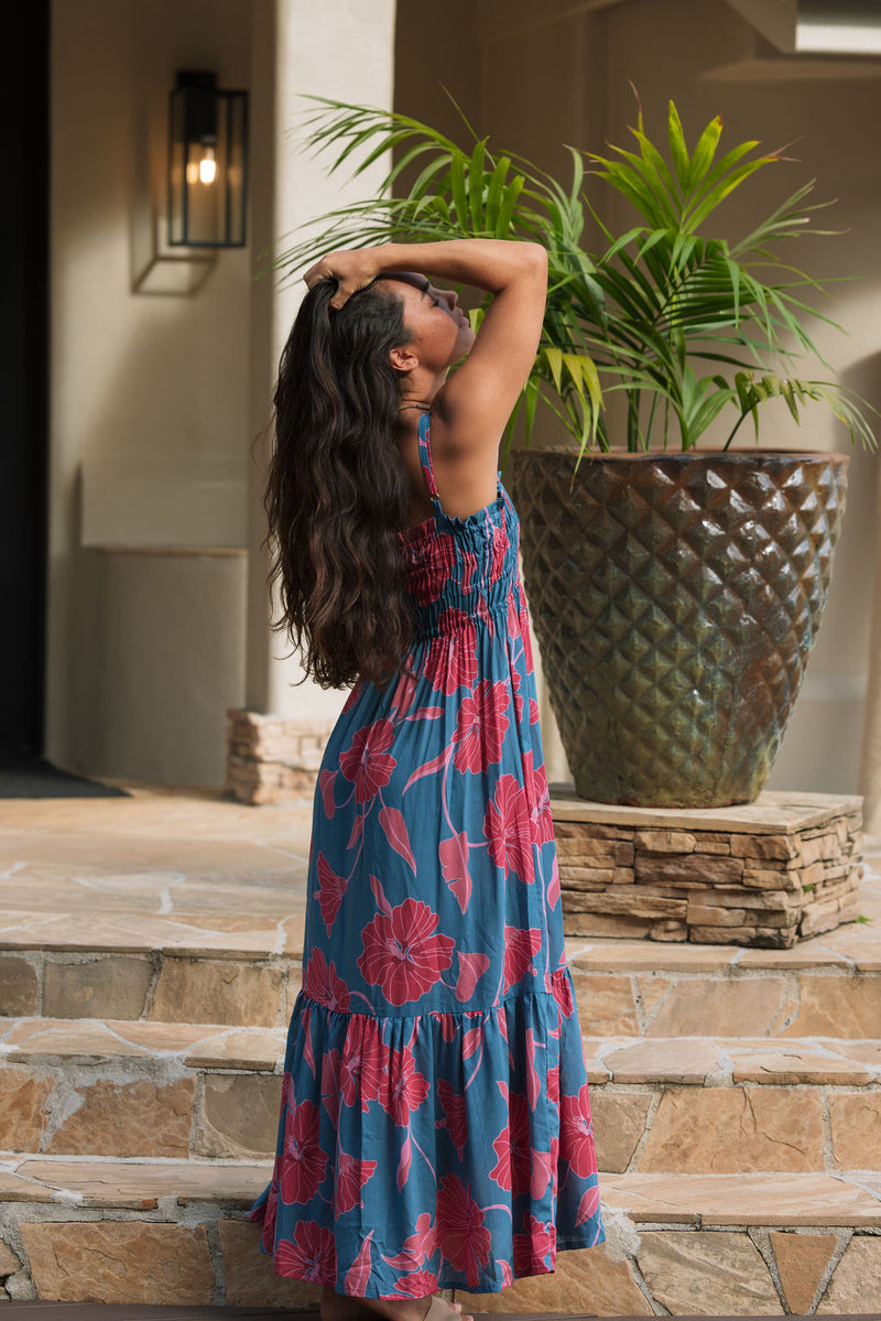 Woman wearing blue sleeveless maxi dress with large pink and red floral print.