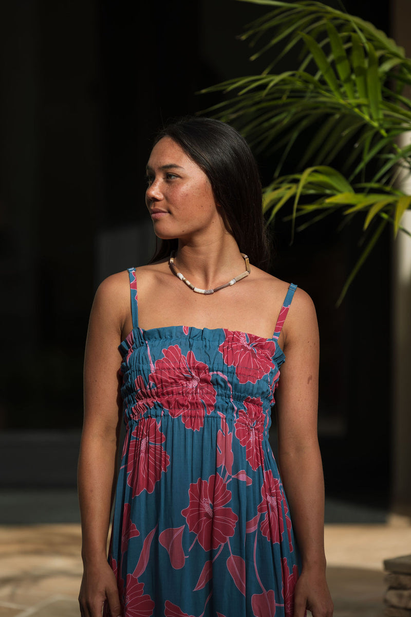 Woman wearing blue sleeveless maxi dress with large pink and red floral print.