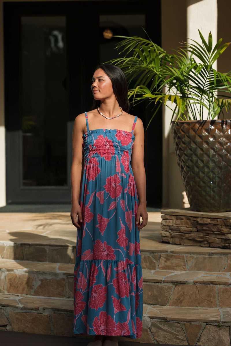 Woman wearing blue sleeveless maxi dress with large pink and red floral print.