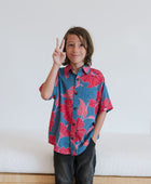 Boy in blue button up shirt with large pink and red floral print.