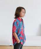 Boy in blue button up shirt with large pink and red floral print.