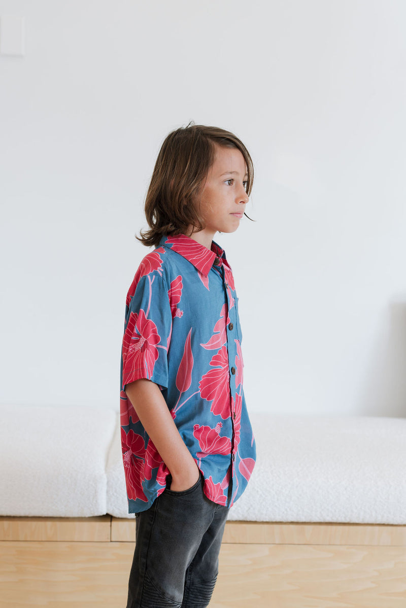 Boy in blue button up shirt with large pink and red floral print.