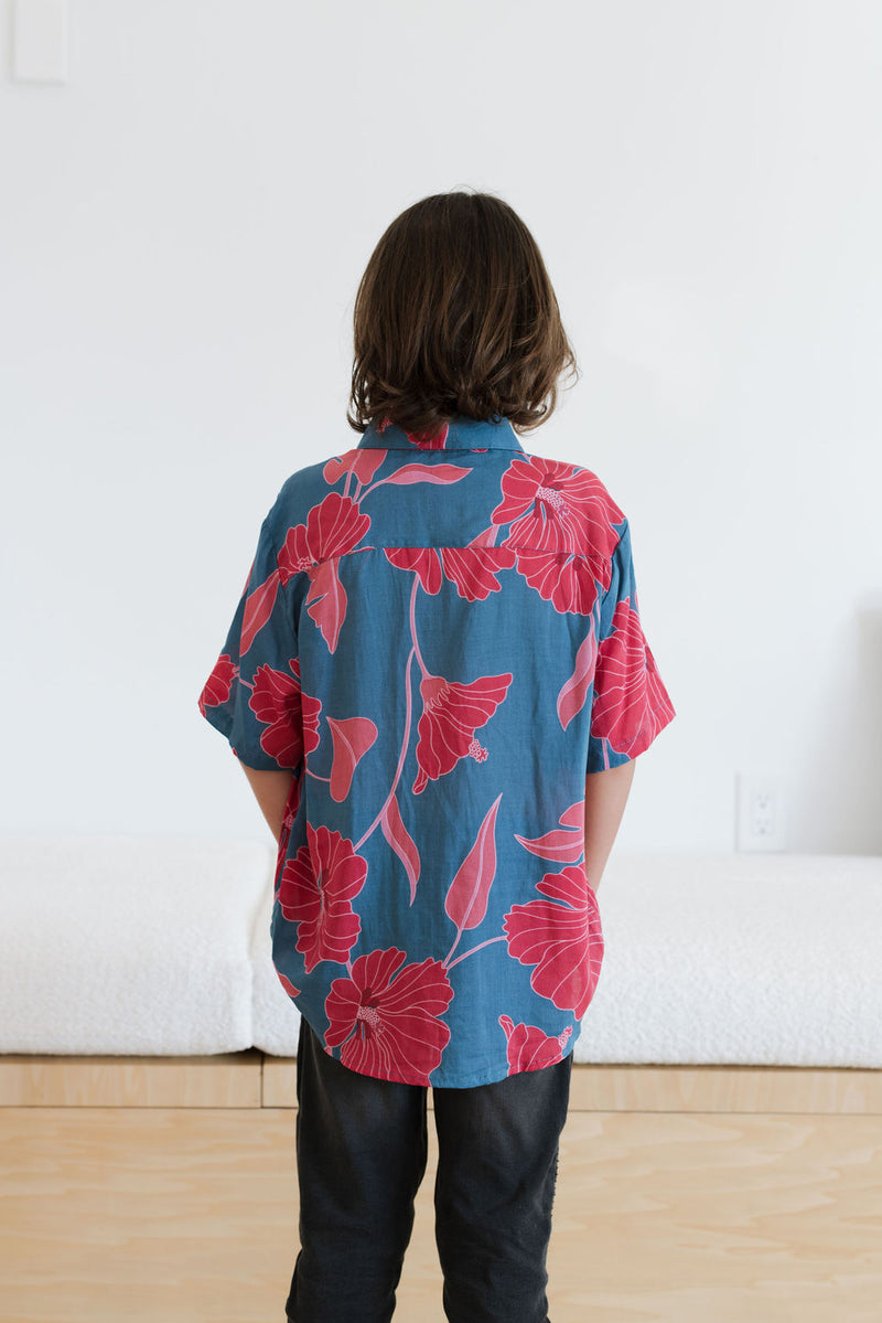 Boy in blue button up shirt with large pink and red floral print.