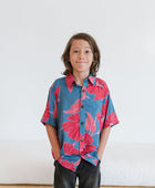 Boy in blue button up shirt with large pink and red floral print.