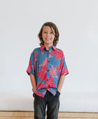 Boy in blue button up shirt with large pink and red floral print.