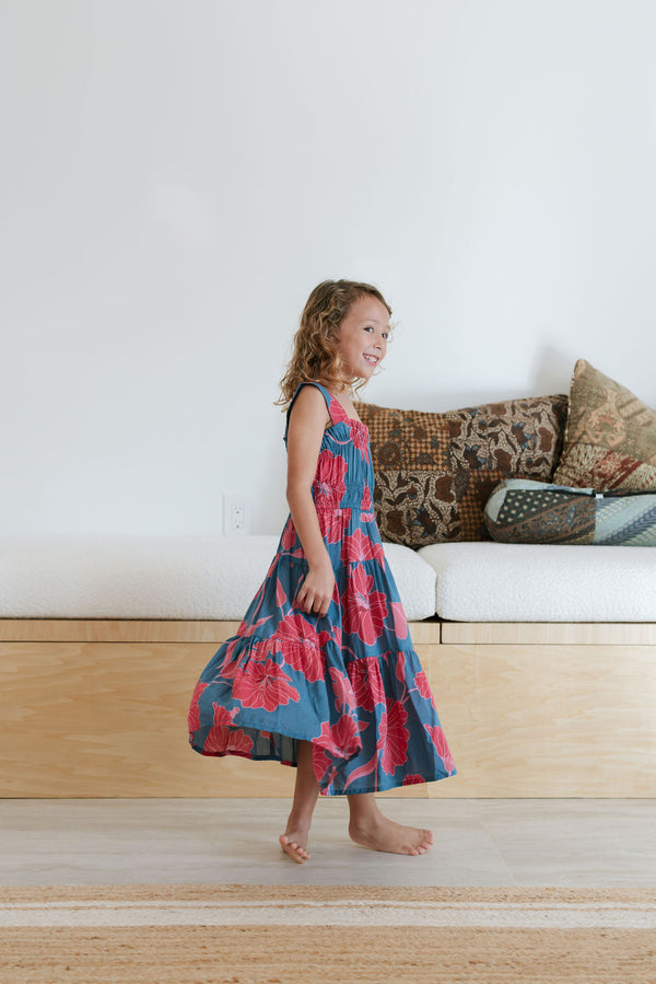 Girl wearing long blue sleeveless dress with large red and pink floral print.