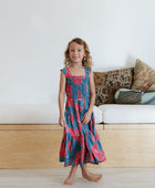 Girl wearing long blue sleeveless dress with large red and pink floral print.