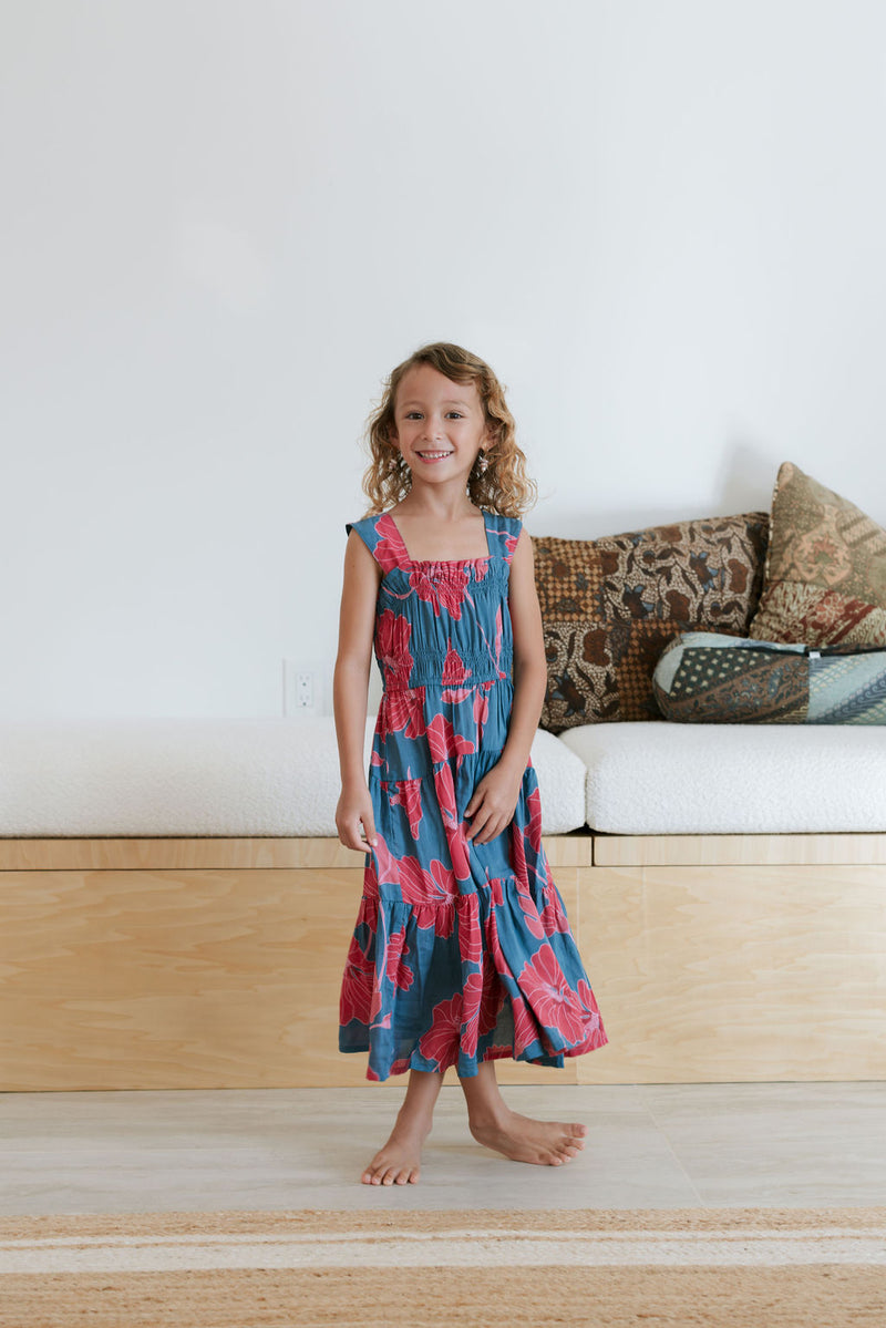 Girl wearing long blue sleeveless dress with large red and pink floral print.