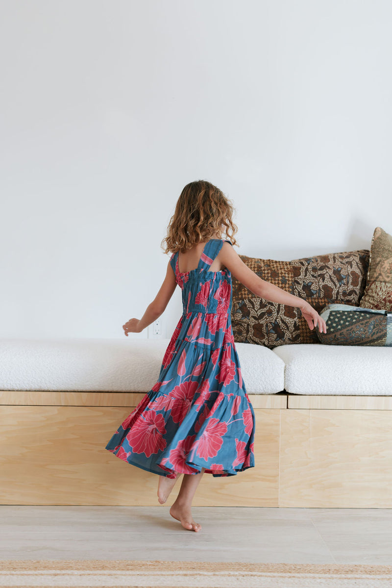 Girl wearing long blue sleeveless dress with large red and pink floral print.