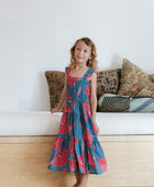 Girl wearing long blue sleeveless dress with large red and pink floral print.