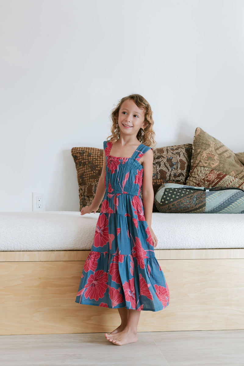 Girl wearing long blue sleeveless dress with large red and pink floral print.