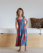 Girl wearing long blue sleeveless dress with large red and pink floral print.