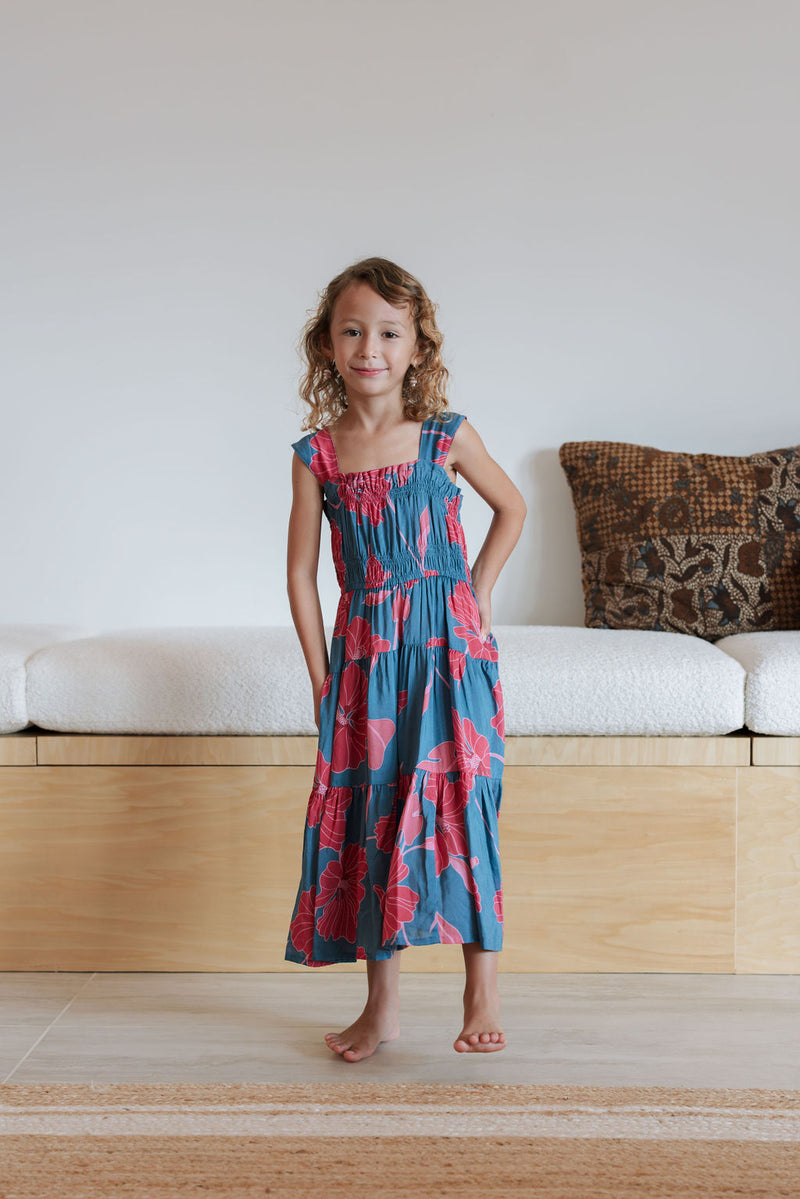 Girl wearing long blue sleeveless dress with large red and pink floral print.